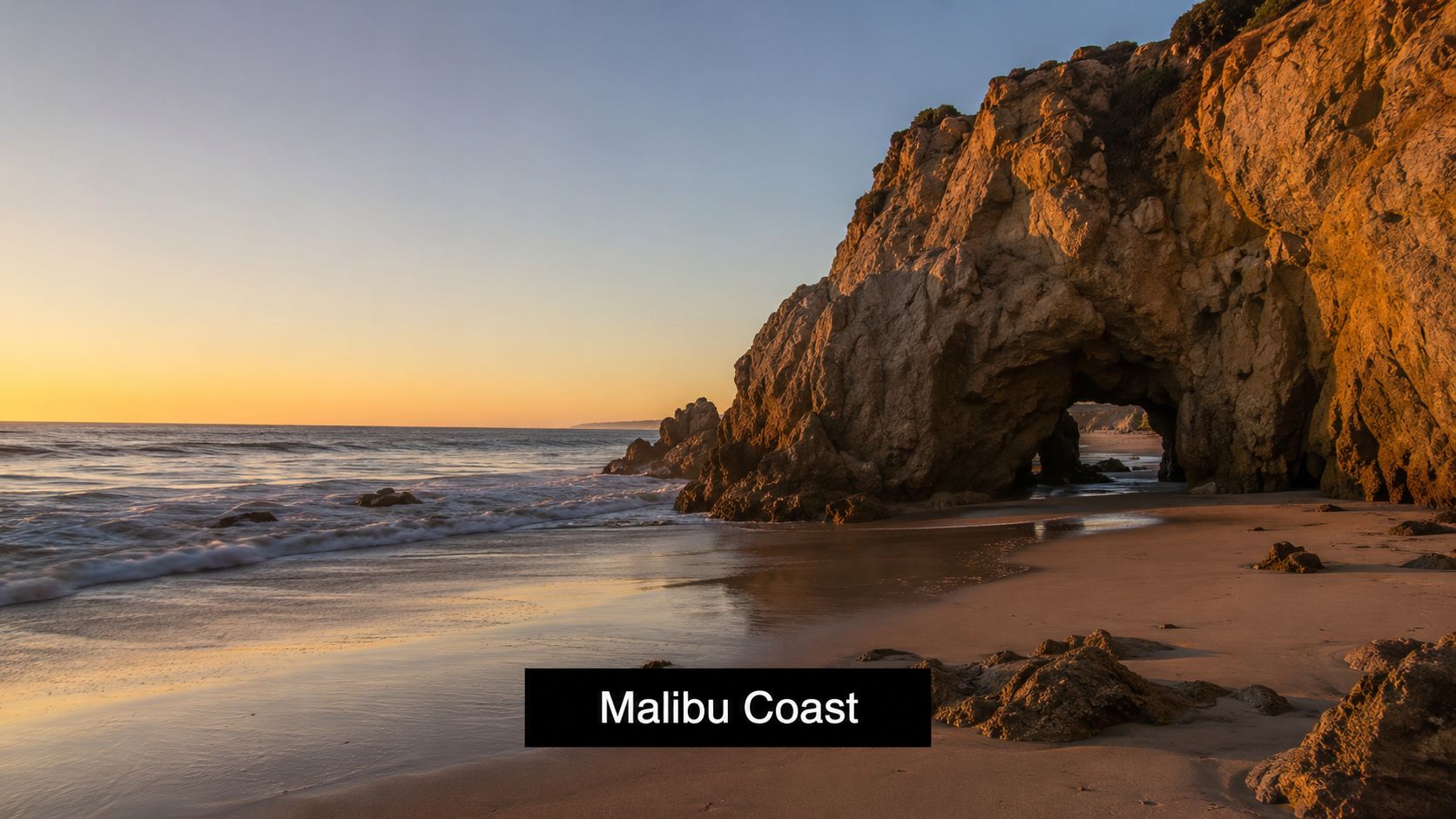 A scenic view of the golden sunset over the rugged cliffs and sandy beach of Malibu Coast.