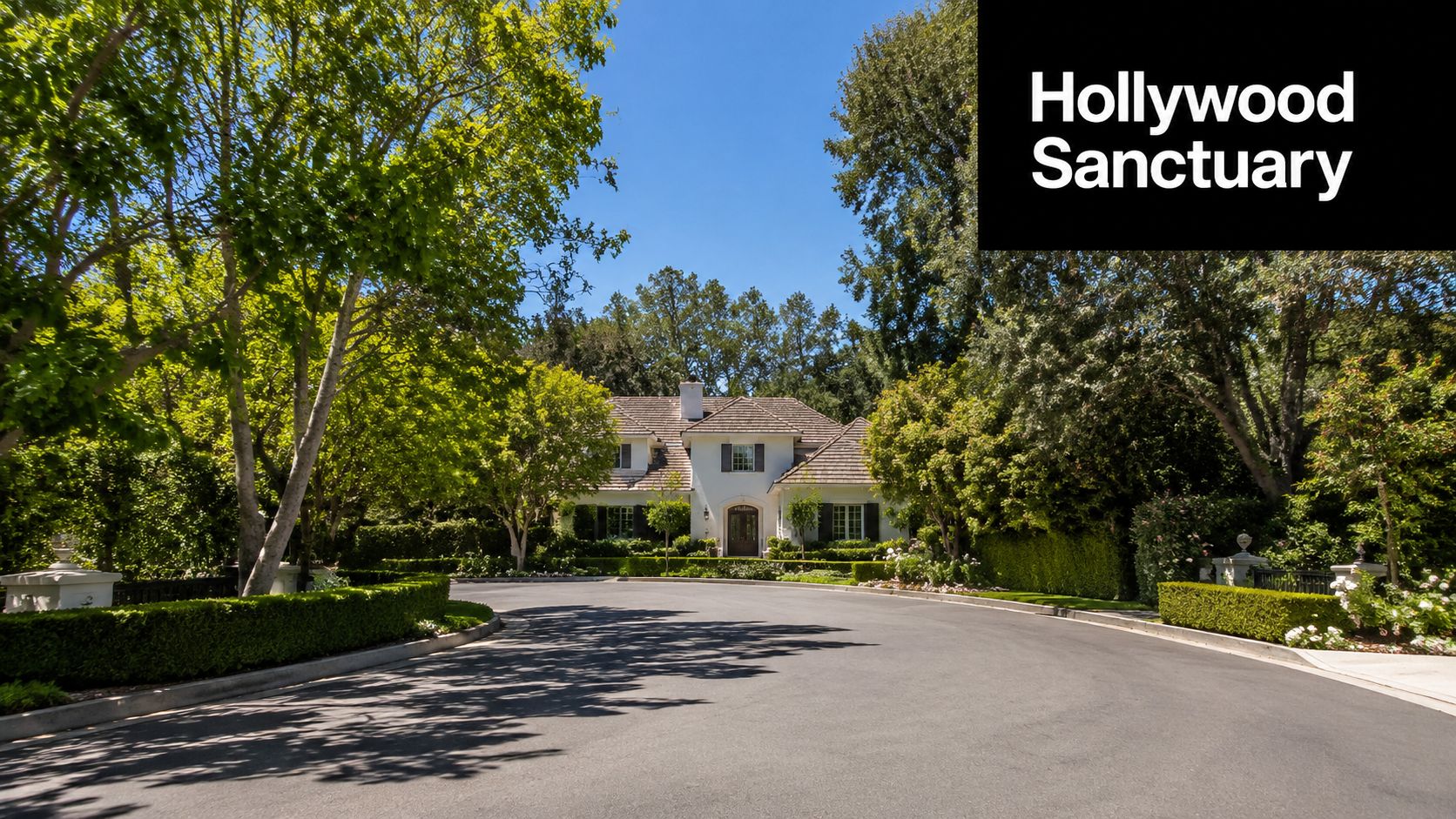 A luxurious white house surrounded by lush green trees and manicured hedges with a private driveway.