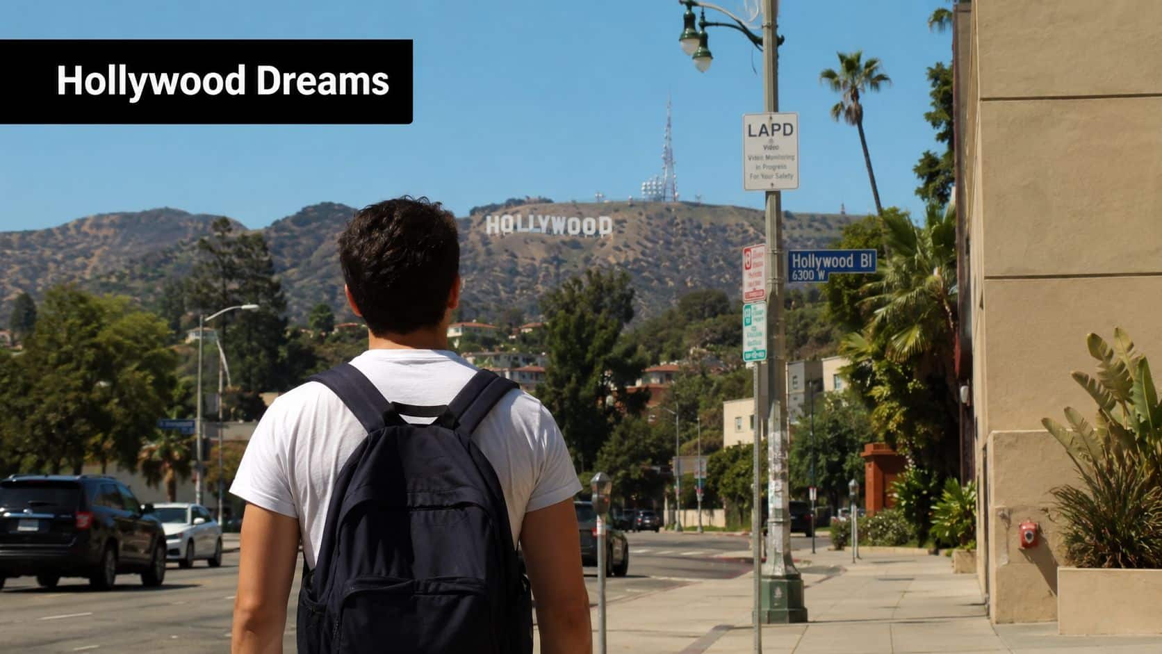 A young man with a backpack stands on a sidewalk looking at the iconic Hollywood Sign