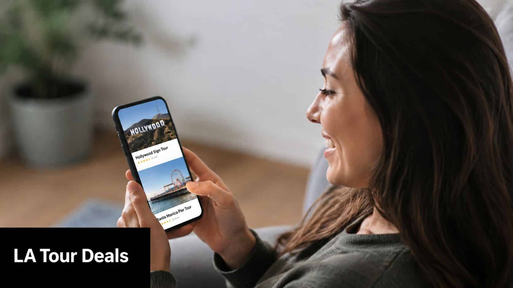 A smiling young woman looking at LA tour deals displayed on her smartphone while sitting comfortably.