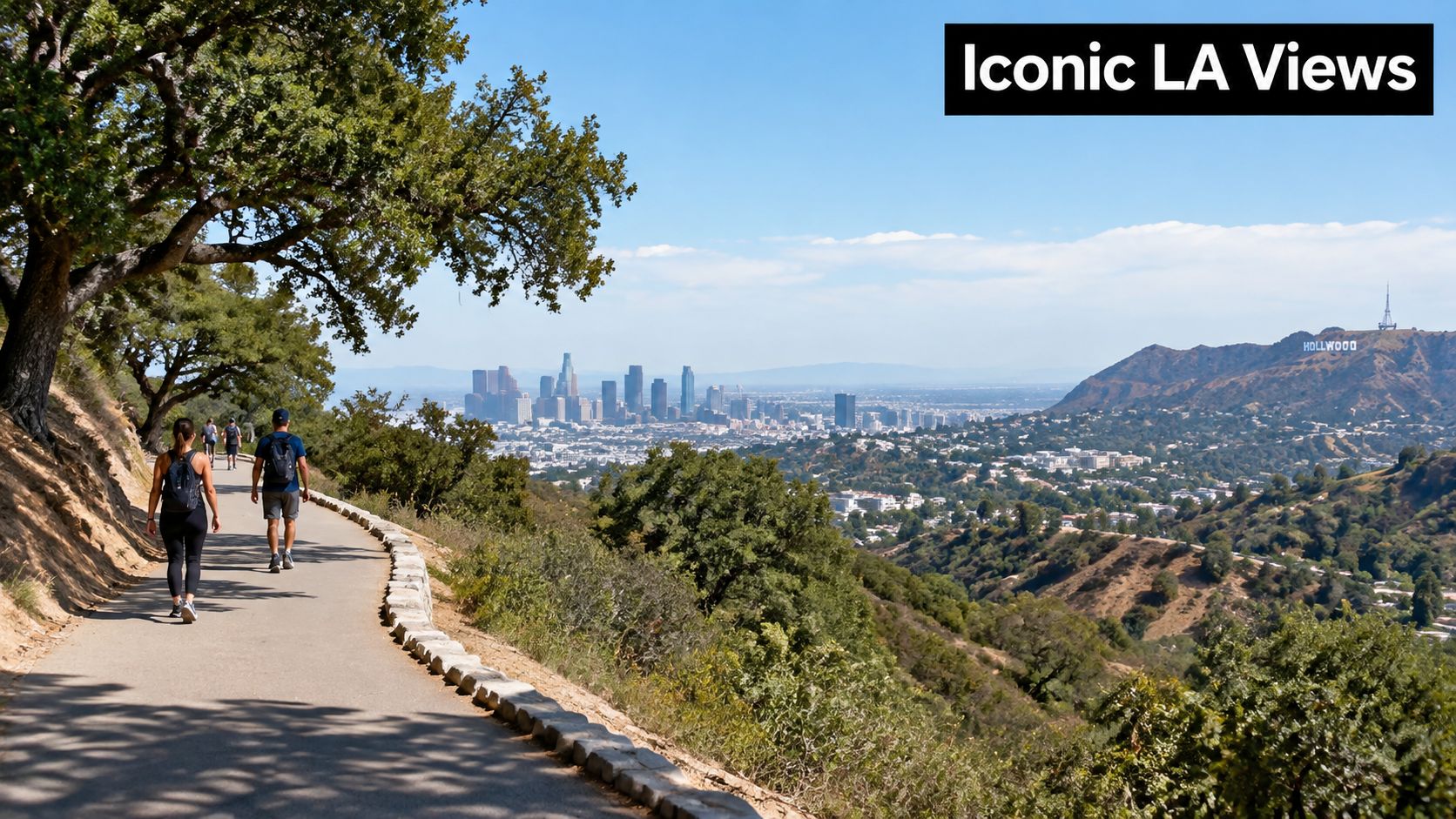 People walking along a scenic paved hiking trail overlooking the Los Angeles skyline and Hollywood sign.